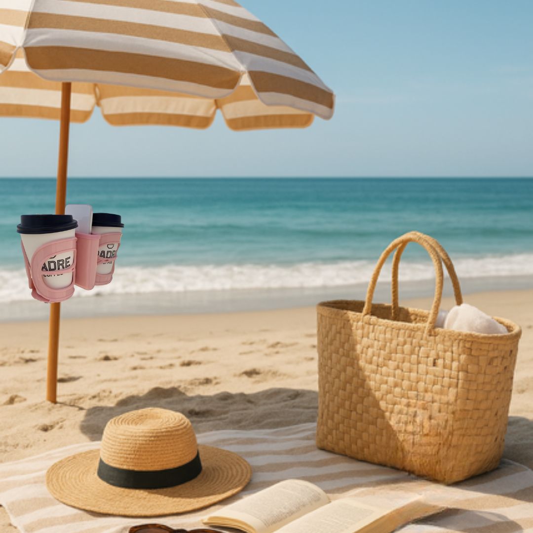Beach scene with striped umbrella, straw hat, bag, and coffee cups in 3-in-1 cup holder on a sandy beach.