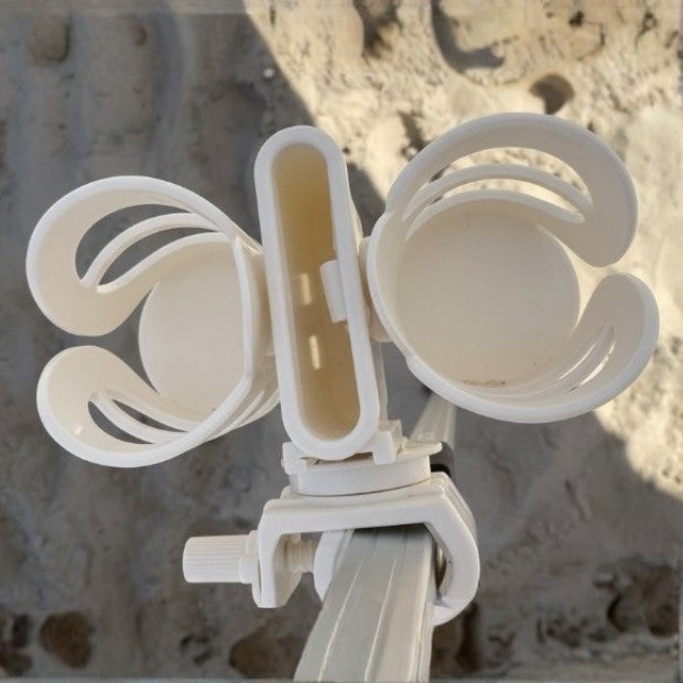 White plastic 3-in-1 beach double cup holder mount attached to a metal pole, shown outdoors against a sandy, sunlit background.