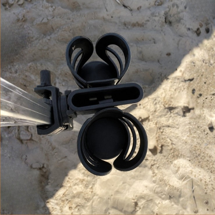 Black plastic 2 cup and phone holder clamp attached to a square beach cabana metal pole, shown outdoors on sandy ground. 
