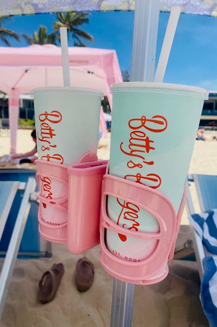 Pink Cup Holder holding 2 drinks and phone at the beach fitted on to beach cabana stand