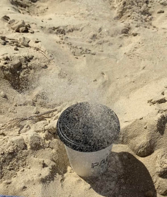 Coffee cup sitting on the sand getting sand thrown on it